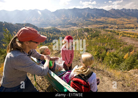 Frau mit Töchtern entspannen Sie auf Bank bei Wanderungen auf Castle Mountain Trail im Herbst, Fernie, BC, Kanada. Stockfoto