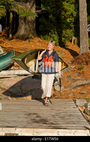 Reife Frau trägt Kanu Quelle See, Algonquin Park, Ontario, Kanada. Stockfoto