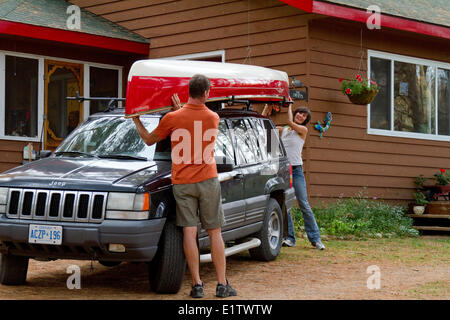 Junges Paar laden Kanu auf dem Dach des Fahrzeugs im Cottage nahe Habichtsbitterkraut See, Muskoka, Ontario, Kanada. Stockfoto