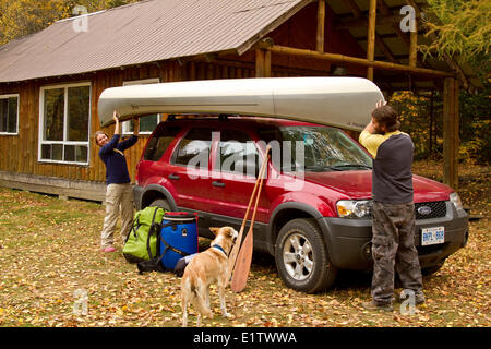 Junges Paar laden Kanu auf dem Dach des Fahrzeugs im Cottage in der Nähe von South River, Algonquin Park, Ontario, Kanada. Stockfoto