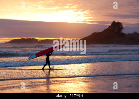 Eine Surfer trägt seinem Surfbrett an Cox Bay bei Sonnenuntergang in der Nähe von Tofino auf Vancouver Island im Clayoquot Sound in British Columbia Kanada Stockfoto