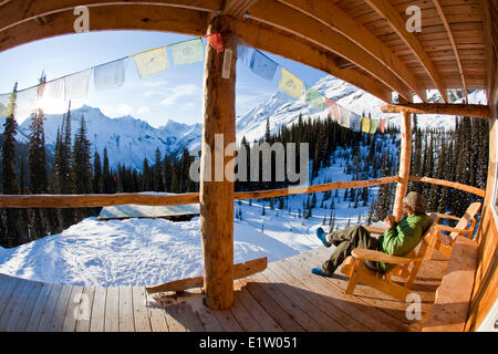 Ein Mann genießen Sie Sonnenaufgang und einen Kaffee im Backcountry-Ski-Hütte. Eisfall Lodge, Golden, BC Stockfoto