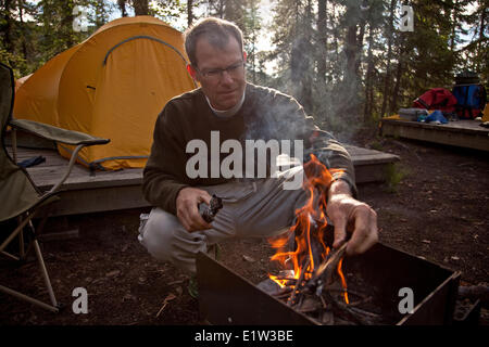 Mann mittleren Alters legt Feuer auf Campingplatz am Virginia Falls Nahanni National Park zu bewahren, NWT, Kanada. Stockfoto