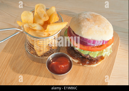 Klassische Burger und Salat mit Beilage Pommes frites oder Chips und Tomatenketchup auf einer Holzplatte Stockfoto