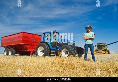 ein Bauernmädchen stehend in Hafer Stoppeln vor einem Traktor und Getreide Wagen während der Ernte, in der Nähe von Dugald, Manitoba, Kanada Stockfoto