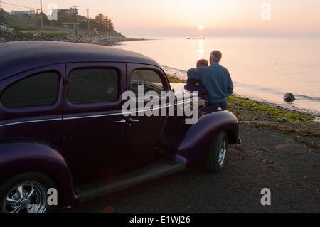 Ein älteres Ehepaar beobachten Sie den Sonnenaufgang am Punkt Holmes Beach von ihren 1939 Ford. Courtenay, BC Stockfoto