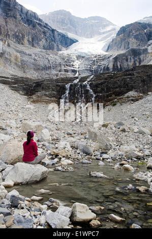 Ein Wanderer sitzt auf einem Felsen neben einem Poolwasser durch den Stanley-Gletscher gespeist. Rauchen Sie in der Nähe ein Lauffeuer hängen über den Bergen. Modell Stockfoto