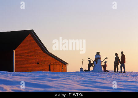 eine Familie machen einen Schneemann vor einem roten Scheune, in der Nähe von Glas, Manitoba, Kanada Stockfoto