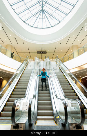 Business-Frau Reiten eine Rolltreppe im Bürogebäude Stockfoto