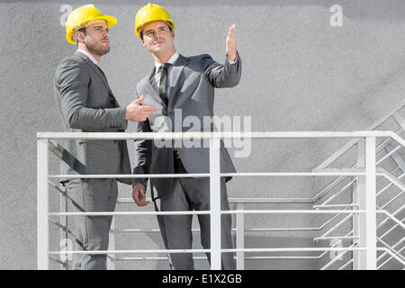Zwei junge Geschäftsleute in harte Hüte diskutieren auf Treppe Stockfoto