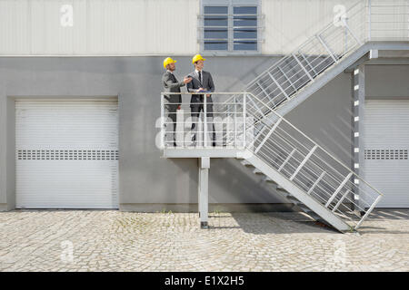 Junge männliche Architekten mit Zwischenablage diskutieren auf Treppe Stockfoto