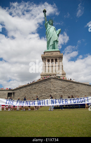 Ein französischer gemeinnütziger Verein namens The Französisch werde nie vergessen, heben einen Banner vor der Statue of Liberty im Rahmen einer Feierstunde zum Gedenken an den 70. Jahrestag des d-Day auf Liberty Island 6. Juni 2014 in New York City, New York. Stockfoto