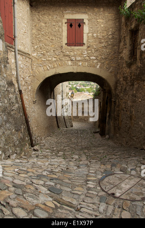 Eine schmale gepflasterte Gasse, Rue St François, führt nach unten aus dem Tour-de-Kamm in die Altstadt, Unterquerung einer mittelalterlichen Torbogen. La Drôme, Frankreich. Stockfoto