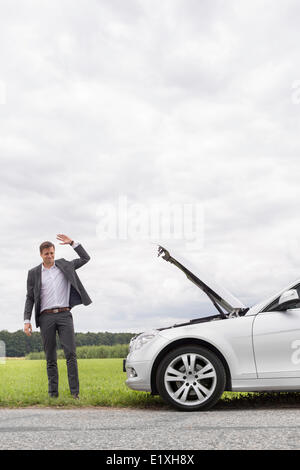 Junger Geschäftsmann winken für Hilfe mit dem Auto kaputt auf Land Stockfoto