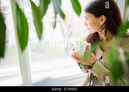 Junge Geschäftsfrau mit Kaffeetasse Blick durch Fenster im Büro Stockfoto