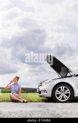 Gesamte Länge der Mitte adult Geschäftsfrau auf Abruf sitzen neben aufgeschlüsselt Auto auf Land Stockfoto