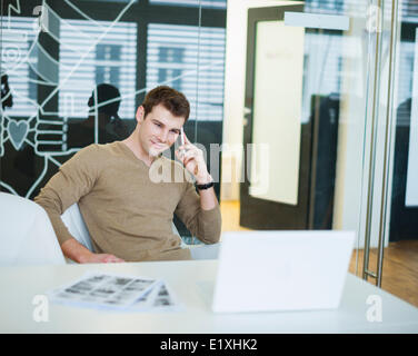 Hübscher junger Geschäftsmann mit Smartphone im Büro Stockfoto