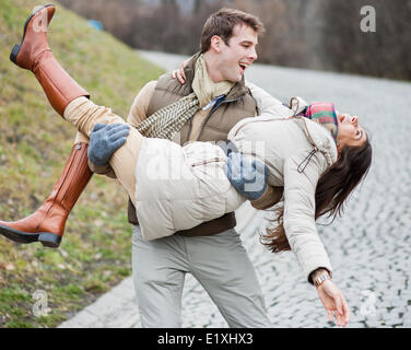 Glücklicher Mann trägt Frau im park Stockfoto