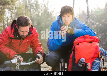 Männliche Wanderer Lesen der Karte während der Freund Kaffeetrinken im Wald Stockfoto