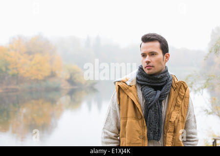 Nachdenklicher junger Mann in warme Kleidung stehend gegen See Stockfoto