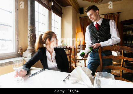 Kellner mit Weinflasche an weibliche Kunden am Tisch im restaurant Stockfoto