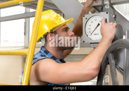 Seitenansicht des jungen männlichen Arbeitnehmer Überprüfung Manometer in der Industrie Stockfoto