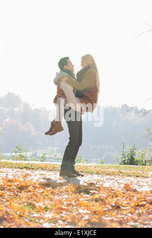 Junger Mann heben Frau im Park im Herbst Stockfoto