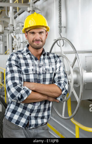 Porträt des Arbeitnehmers mit verschränkten Armen stützte sich auf großes Ventil in der Industrie Stockfoto