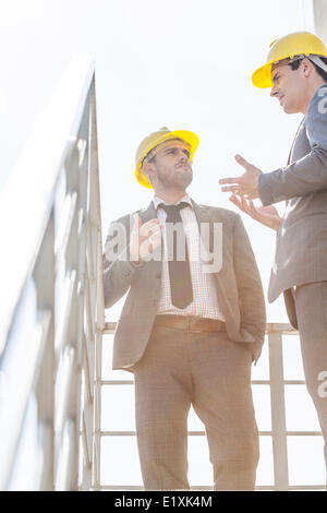 Niedrigen Winkel Ansicht der männlichen Jungunternehmer in harte Hüte, die Diskussion auf Treppe gegen klaren Himmel Stockfoto
