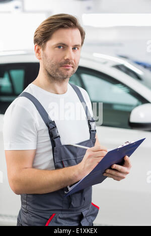 Porträt des zuversichtlich Kfz Mechaniker Schreibens auf Zwischenablage in Werkstatt Stockfoto