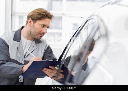 Mitte Erwachsener reparieren Sie Arbeitnehmer schriftlich auf Zwischenablage während der Prüfung Auto in Werkstatt Stockfoto