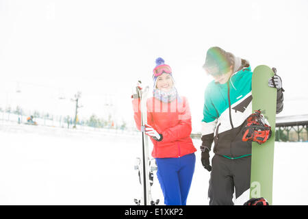 Glückliches junges Paar mit Snowboard und Ski im Schnee Stockfoto