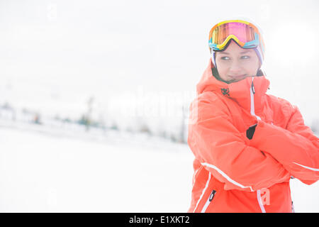 Glückliche junge Frau in warme Kleidung stehend Arme gekreuzt auf schneebedecktes Feld Stockfoto