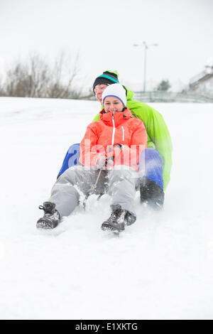 Voller Länge des jungen Paares auf Schnee Rodeln bedeckt land Stockfoto