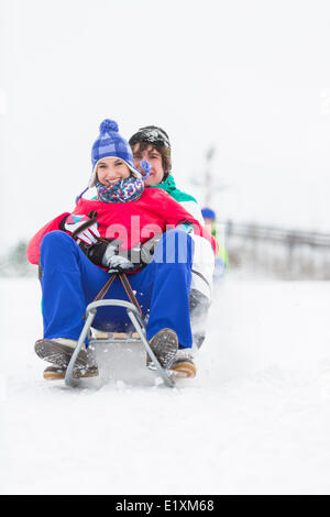 Voller Länge Porträt des jungen Paares Schlittenfahrt im Schnee genießen Stockfoto