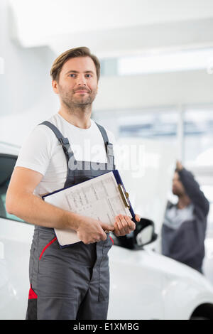 Porträt von zuversichtlich männliche Automechaniker mit Zwischenablage in Auto-Reparatur-Speicher Stockfoto