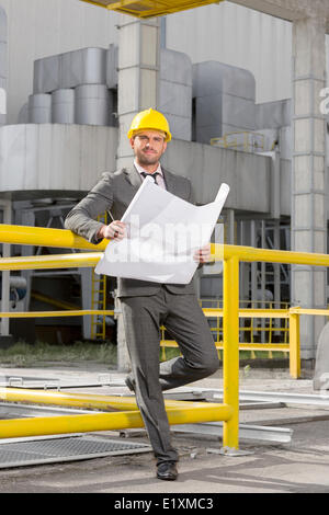 In voller Länge Portrait von jungen männlichen Architekten mit Blaupause außerhalb Industrie Stockfoto