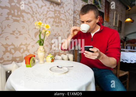 Mann mit Kaffee beim Lesen von SMS auf Handy im café Stockfoto