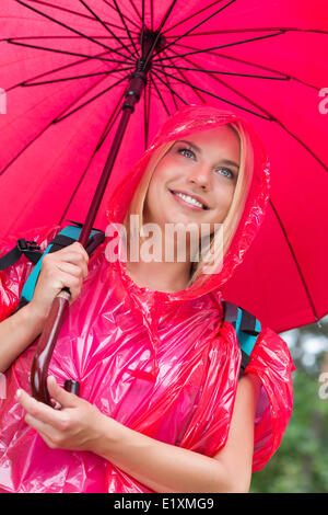 Lächelnd weibliche Wanderer im roten Regenmantel mit Regenschirm Stockfoto