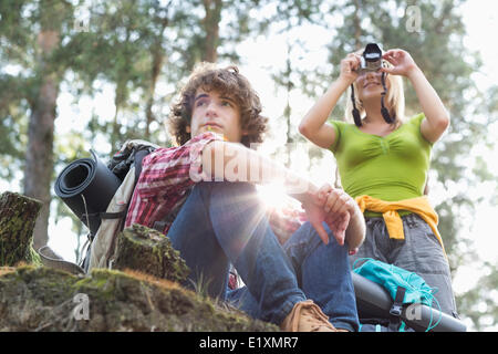 Junge weibliche Wanderer fotografieren durch Digitalkamera während Mann wegsehen im Wald Stockfoto