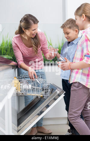 Glückliche Mutter und Kinder platzieren Gläser in Spülmaschine