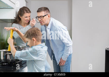 Eltern schmeckendes Essen während Sohn Zubereitung von Speisen in der Küche Stockfoto