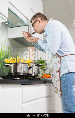 Mid-Adult Mann schmeckendes Essen beim Kochen in der Küche Stockfoto