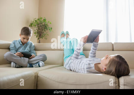 Geschwister, die mit Technologien zu Hause auf sofa Stockfoto