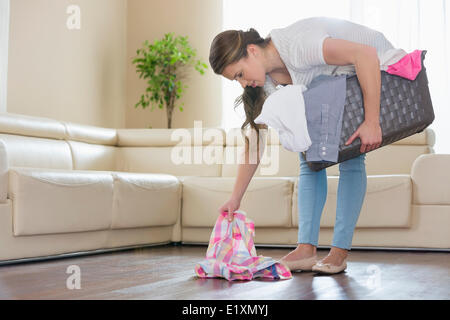 Frau mit Wäschekorb Kommissionierung Kleidung vom Boden im Wohnzimmer Stockfoto