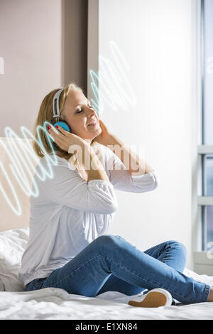 Entspannte Mitte Erwachsene Frau hören von Musik über Kopfhörer auf Bett Stockfoto
