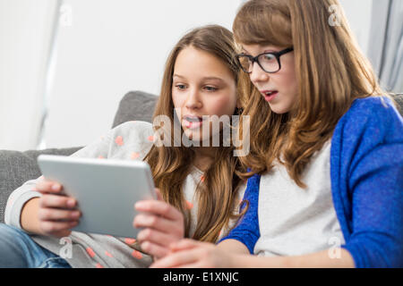 Schockiert Schwestern mit digital-Tablette zu Hause auf sofa Stockfoto