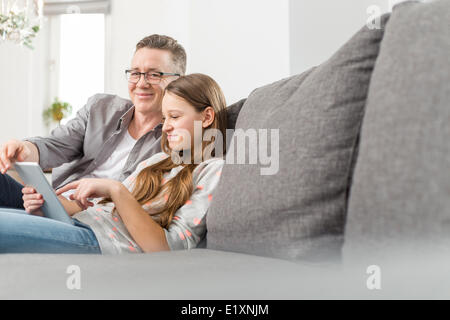 Porträt der lächelnden Vater Tochter zu unterstützen, im Umgang mit digitalen Tablet zu Hause auf sofa Stockfoto