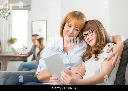 Liebevolle Mutter und Tochter mit digital-Tablette mit Familie sitzt im Hintergrund zu Hause Stockfoto