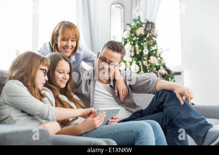 Familie mit Tablet-PC auf Sofa mit Weihnachtsbaum im Hintergrund Stockfoto